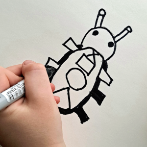 The child holds a black marker and draws a beetle-like bug on white paper.