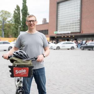 Henkilö rautatieaseman edustalla kaupunkipyörän kanssa.